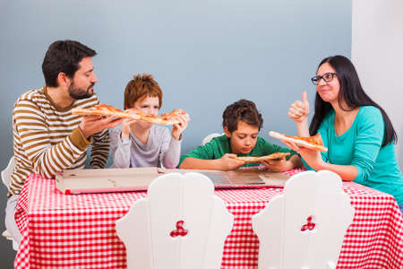 Parents and their two sons are eating pizza at home.の写真素材
