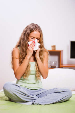 Young woman with allergy problem is sitting in her bed and blowing nose.の写真素材