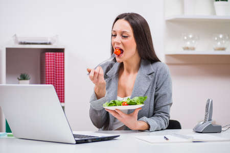 Young businesswoman is eating salad in her office.の写真素材