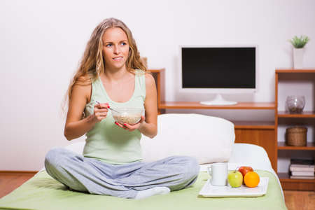 Young woman sitting in her bed and eating oatmeal. It's time for breakfast.の写真素材