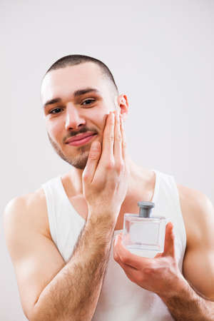 Young man is applying aftershave to his face.の写真素材