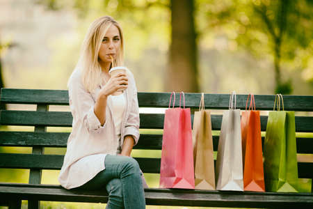 Young happy woman sitting in park after shopping and drinking coffee.  Intentionally toned.の写真素材