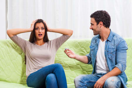 Young couple is sitting at sofa at home. Man is proposing to his woman.の写真素材