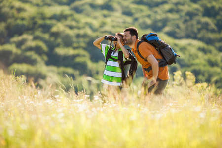 Father and son are hiking in nature in summer. They are using binoculars.の写真素材