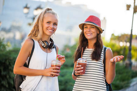 Two happy women are having nice time together in the city. They are drinking smoothie.の写真素材