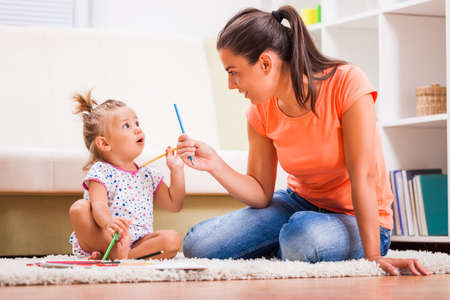 Mother and daughter in their home. Little girl is learning to draw.の写真素材
