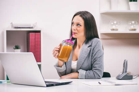 Young businesswoman is drinking smoothie in her office.の写真素材