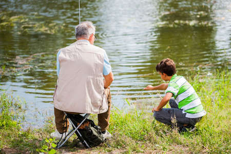 Grandfather and grandson are fishing on sunny day.の写真素材