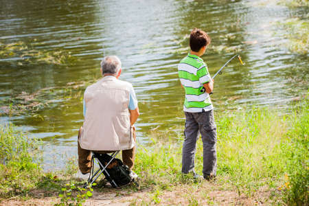 Grandfather and grandson are fishing on sunny day.の写真素材