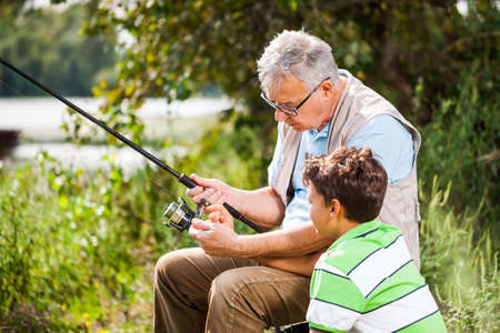 Grandfather and grandson are fishing on sunny day.の写真素材
