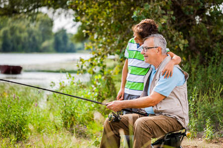 Grandfather and grandson are fishing on sunny day.の写真素材