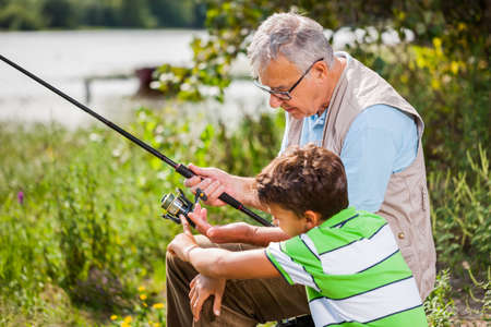 Grandfather and grandson are fishing on sunny day.の写真素材