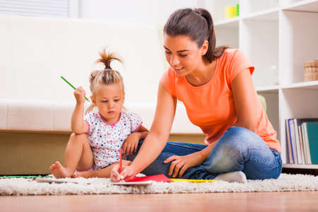 Mother and daughter in their home. Little girl is learning to draw.の写真素材