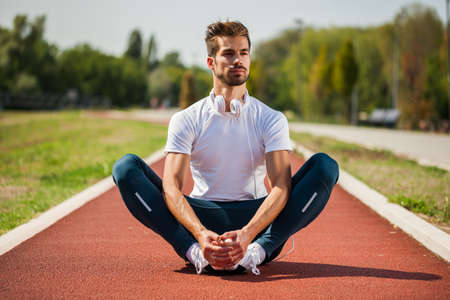 Young man is exercising on sunny day. He is stretching his body.