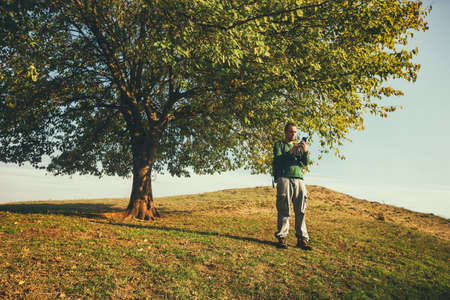 Man is hiking in nature on sunny day. He is looking at map on his phone.の写真素材