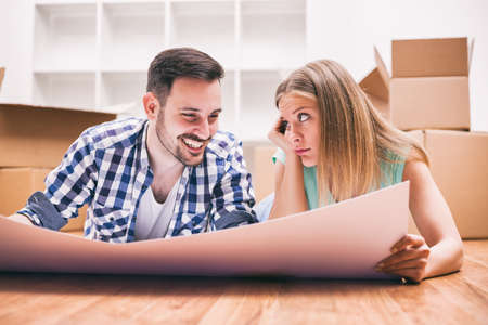 Young couple is moving in their new home. They are looking at apartment blueprint.の写真素材