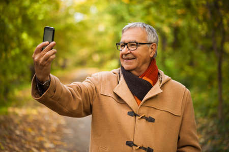 Happy senior man taking selfie in park in autumn.