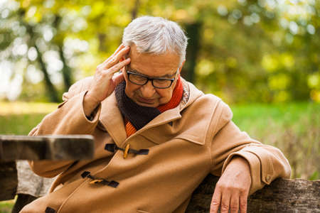 Senior man sitting in park and having headache.の写真素材