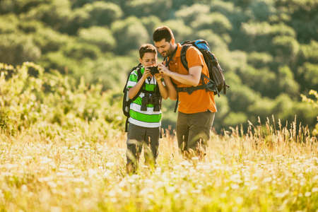 Father and son are hiking in nature in summer. Boy is photographing.の写真素材