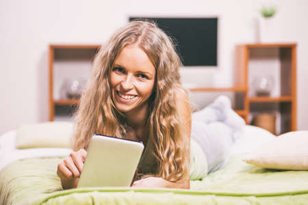 Young woman is lying in bed and using digital tablet.の写真素材