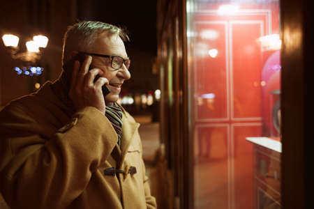 Senior man is looking at store front and talking on phone.の写真素材