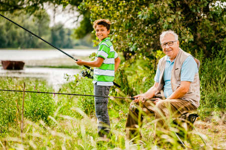 Grandfather and grandson are fishing on sunny day.の写真素材