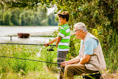 Grandfather and grandson are fishing on sunny day.の写真素材