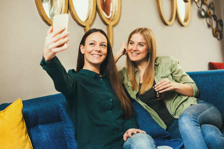 Two happy women are sitting in cafe and taking selfie.の写真素材