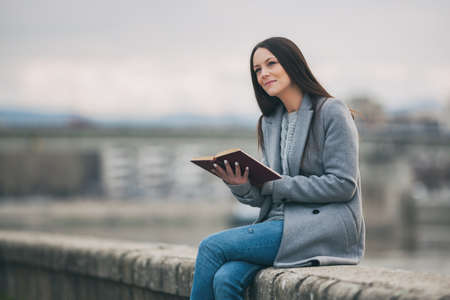 Young woman is reading book outdoor on cloudy day.の写真素材