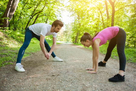 Couple is exercising in park. They are stretching bodies.