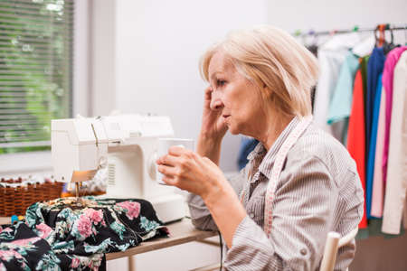 Adult woman is sewing in her studio. She is tired.の写真素材
