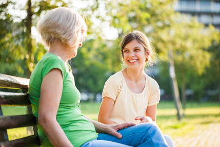 Grandmother and granddaughter are sitting in park and talking.の写真素材