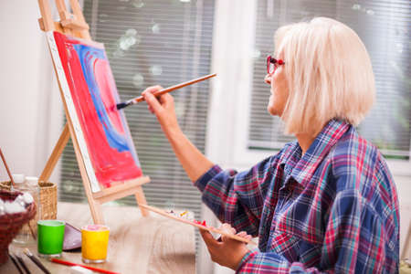 Elderly woman is painting in her home. Retirement hobby.の写真素材