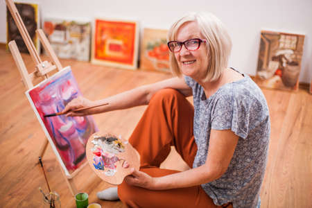 Elderly woman is painting in her home. Retirement hobby.