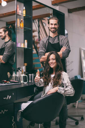 Young woman getting new hairstyle at professional hair styling saloon. She is very satisfied.
