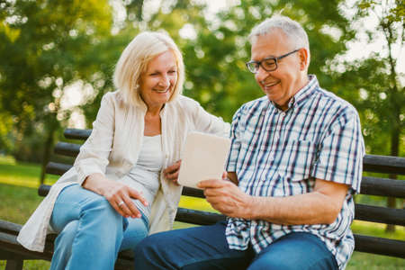 Happy senior couple is using digital tablet in park.の写真素材