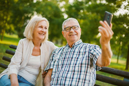 Happy senior couple is taking selfie in park.の写真素材