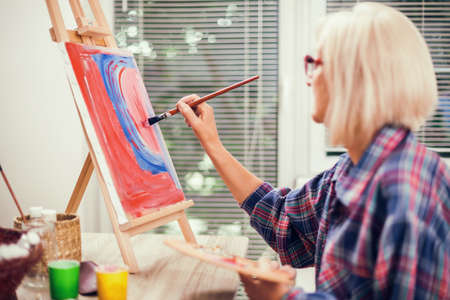 Elderly woman is painting in her home. Retirement hobby.の写真素材