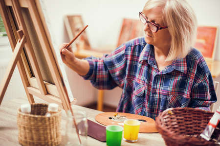 Elderly woman is painting in her home. Retirement hobby.の写真素材