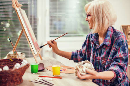 Elderly woman is painting in her home. Retirement hobby.の写真素材
