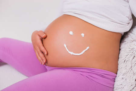 Close up of pregnant woman's stomach with smiley drawing.の写真素材