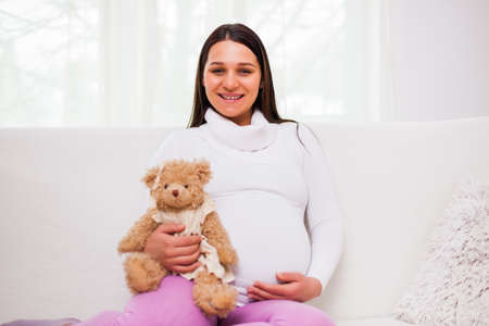 Happy pregnant woman sitting at sofa in home.の写真素材