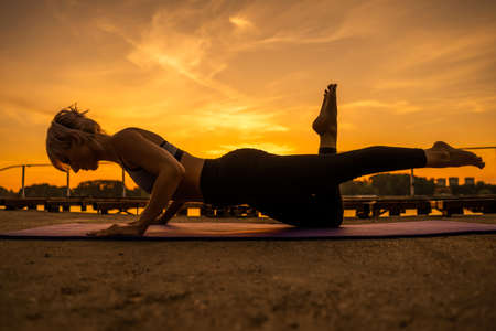 Woman exercising pilates in sunset. One legged ladies push up exercise.