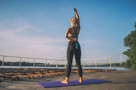 Woman exercising pilates with elastic band on sunny day.