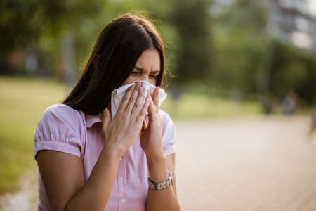 Woman with allergy symptom blowing nose in park.の写真素材