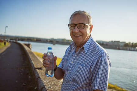 Outdoor portrait of senior man who is holding bottle of water.の写真素材