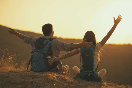 Young happy couple is hiking in mountain and looking at sunset.