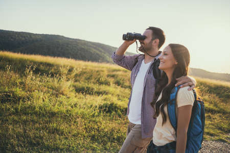Happy couple is hiking in mountain. They are watching nature with binoculars.の写真素材