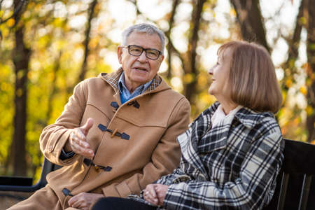 Senior couple is sitting on bench in park and enjoying autumn.の写真素材