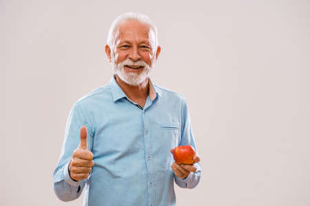 Portrait of cheerful senior man who is holding apple and smiling.の写真素材